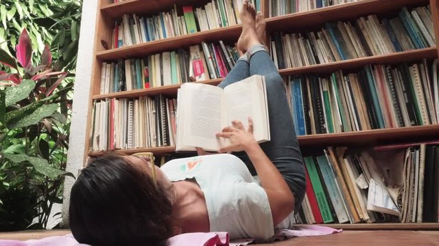 Hispanic woman reading liying on the floor of the library. 4k