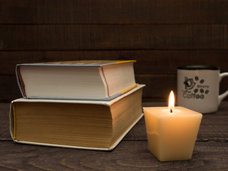 Books, a cup of strong coffee and a candle on a wooden table