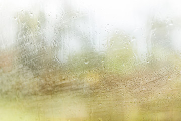 Macro closeup of wet car glass window with rain falling stormy weather, green blurred trees forest in autumn