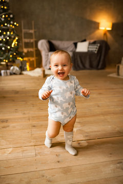Little baby boy laughs cheerfully and walks on plank floor.