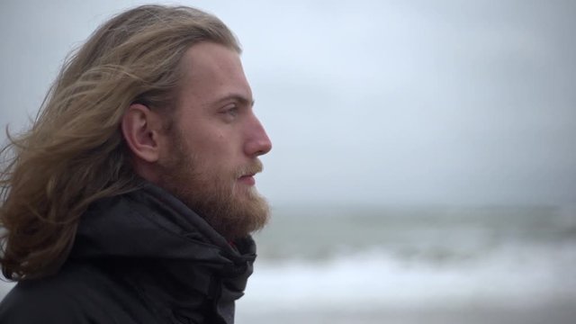 Portrait in profile of manly male explorer with long brown hair taking pleasure in force of nature breathing fresh cold air looking ahead in slow motion