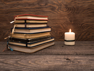 A pile of notebooks and a candle on a wooden table