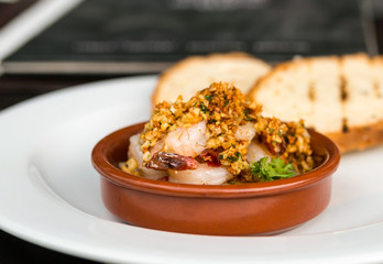 fried shrimp covered with crushed nuts with onions in a brown cream bowl on a grilled toast background