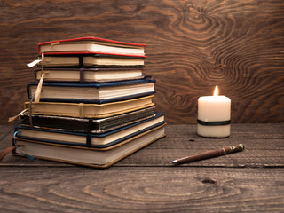 A stack of notebooks, a pen and a candle on a wooden table