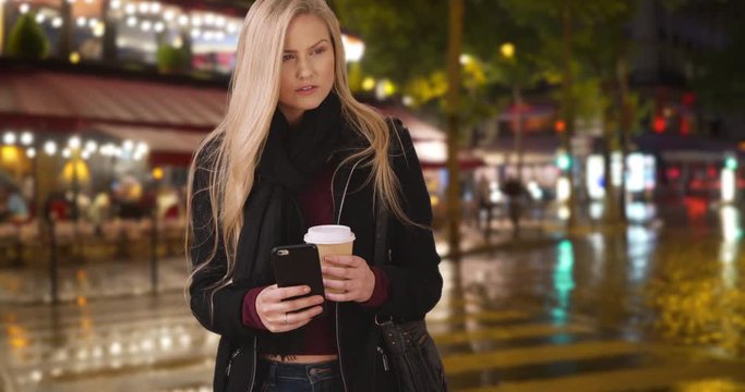 White young woman using phone while out in city on rainy night