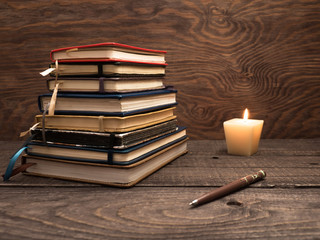 A stack of notebooks, a pen and a candle on a wooden table
