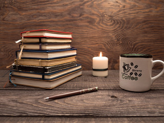 Notebooks, a pen, a candle and a cup of strong coffee on a wooden table