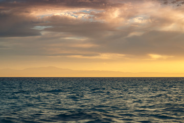 Crimson sunset on the shore of the orange sky and calm sea witt view at the mountains