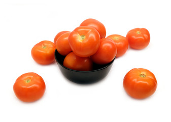 Many ripe red appetizing tomatoes in black round bowl and scattered on white background front view closeup