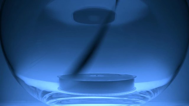 In the glass bowl lies a coil VHS and the magnetic tape pull up on blue background. Closeup. Slow mo, slo mo, slow motion, high speed camera, 240fps, 250fps
