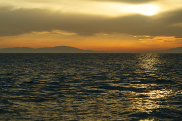 Crimson sunset on the shore of the orange sky and calm sea witt view at the mountains