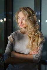 Beautiful girl with long curly blonde hair posing with crossed hands. Natural makeup and perfect skin.