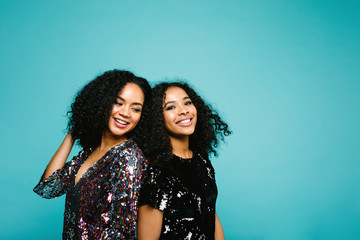 Portrait of a two mixed race women standing back to back against blue background