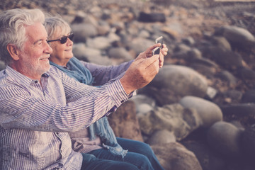 couple of adults sitting at the beach looking at the phone and taking pictures 