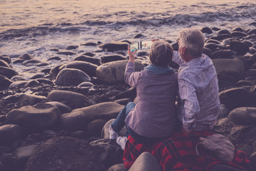 Fototapeta premium couple of adults sitting at the beach looking at the phone and taking pictures 