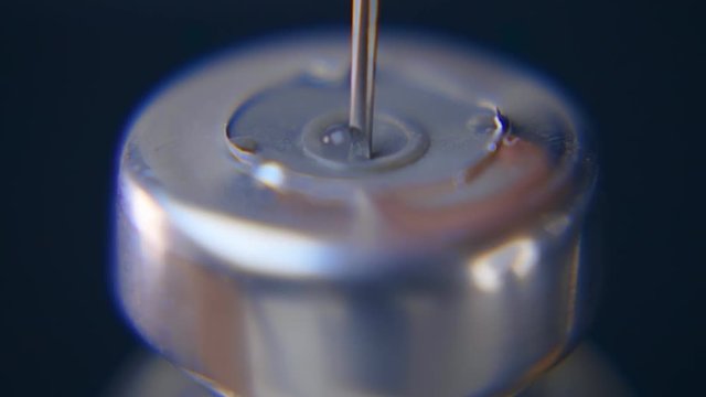 Syringe needle pierces the rubber stopper of the glass vial and diluted from saline the crystals of the medicament on a black background. Slow motion, slo mo, high speed camera, 240fps, 250fps