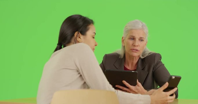 A young employee shows her boss a new strategy on her mobile phone on green screen. On green screen to be keyed or composited. 