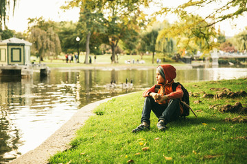 boy sitting on the shore of a pond. child resting near a city pond with ducks. copy space for your text