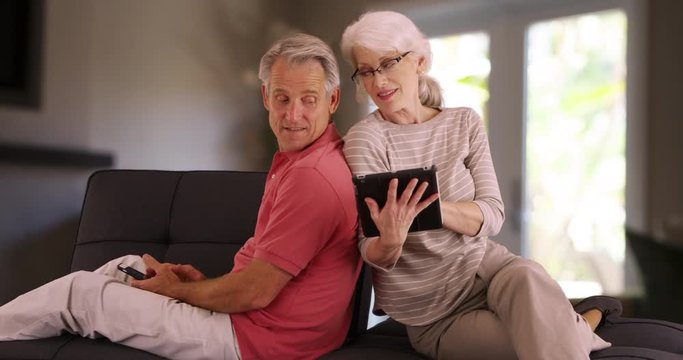 Senior couple using devices on couch at home