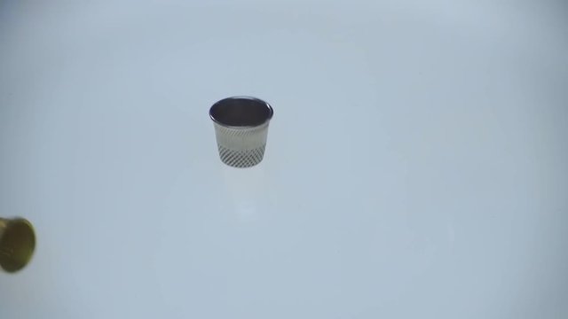 Three thimbles fall on a glossy white luminous surface. Macro. Closeup. Slow mo, slo mo, slow motion, high speed camera, 240fps, 250fps
