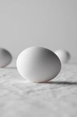 Close-up of white egg on a white linen tablecloth background.