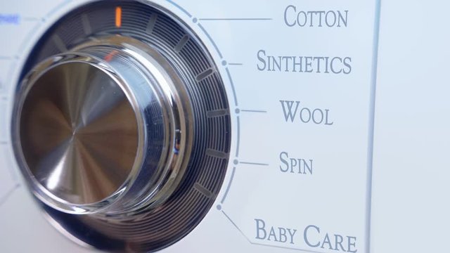 The washing machine turns on, the LEDs light up, the hand twists the shiny switch of the operating modes of the machine. Closeup
