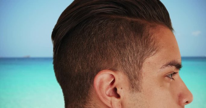 Close up of handsome Latin male with cool undercut standing by ocean 
