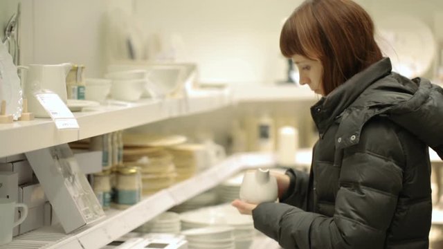 Young woman is choosing crockery at shop
