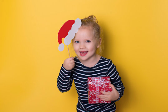 Pretty smiling  little girl with santa hat and gift box on yellow background
