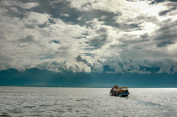 A boat advances on Lake Erhai towards the city of Dali while the clouds cling to the surrounding...