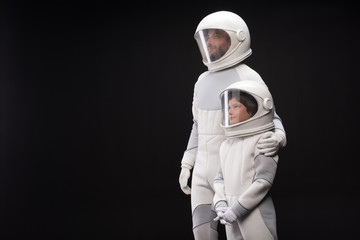 Inseparable. Cheerful father and his interested son wearing white helmet with full armor are standing together with smile. Man is looking forward while hugging boy. Isolated with copy space