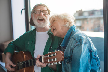 Carefree day. Portrait of mature male and female singing favorite song while playing on guitar at...