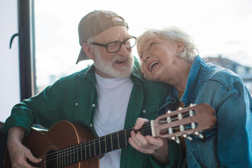 Favorite song. Portrait of two happy pensioners looking to each other with love. Man is playing on musical instrument