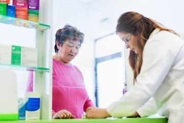 Female pharmacist discusses prescription medication with senior customer at pharmacy