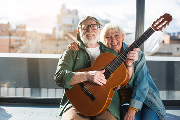 Remember youth. Charming married senior man and woman enjoying playing on musical instrument. They are looking at camera while husband is putting out tongue. Copy space