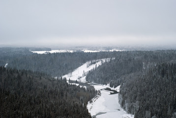 a view of the winter valley of a frozen river amidst snow-covered wooded hills from a bird's eye view
