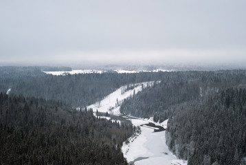 Naklejka premium a view of the winter valley of a frozen river amidst snow-covered wooded hills from a bird's eye view