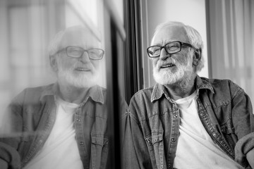 Black-and-white portrait of wrinkled bearded positive pensioner observing life at the street