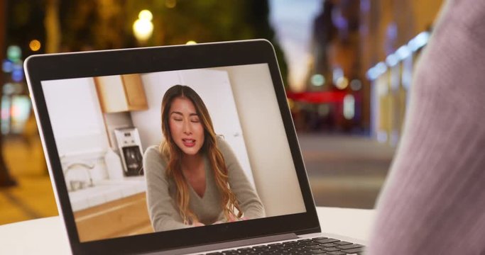 Woman on Champs-Elysees avenue video chatting with Asian female on laptop