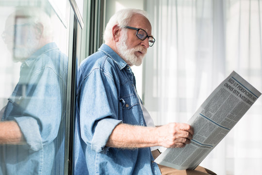 Smart occupation. Side view of interested pensioner reading favorite column in fresh newspaper