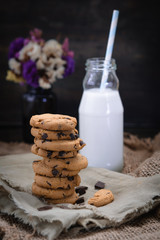 Chocolate chip cookies with milk on paper and rustic wooden table