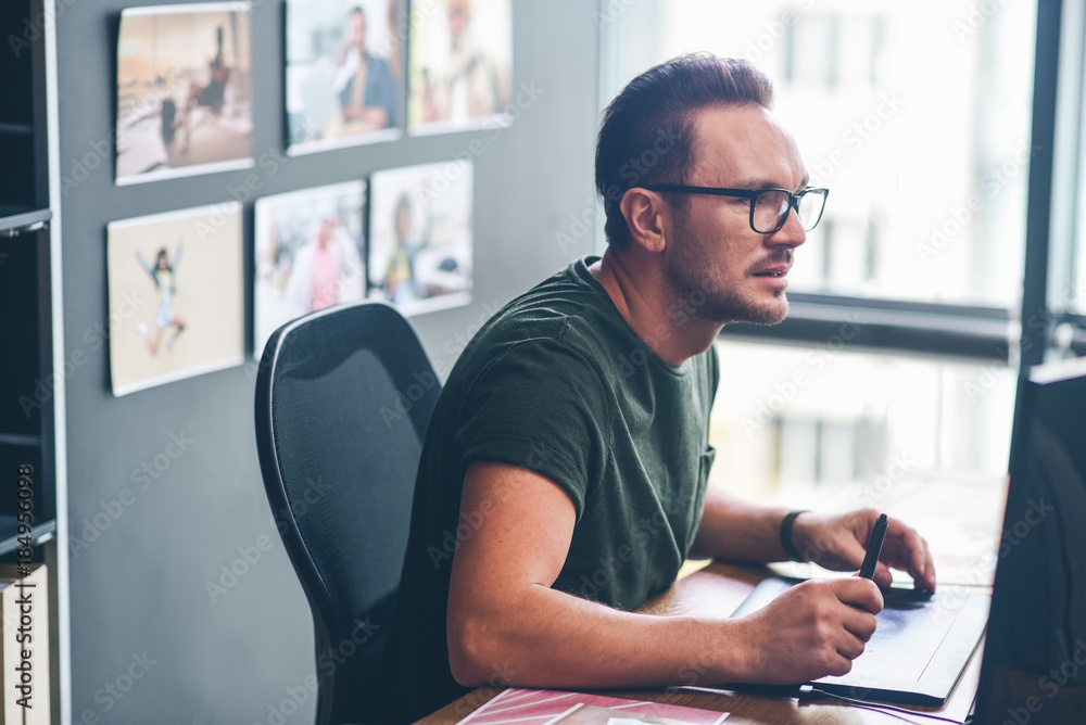 Poster side view serene unshaven man drawing on digital device while looking at gadget. he sitting at table