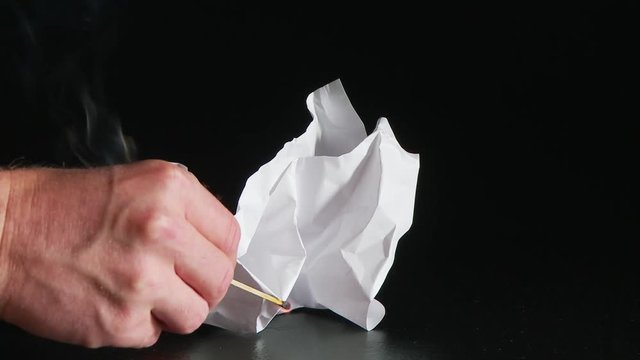 person lighting white ball of paper with match