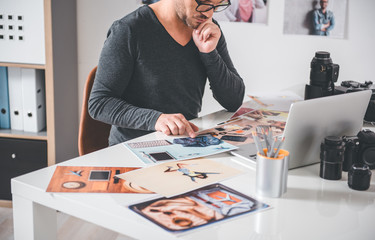 Serene bearded man watching at pictures while locating at table in room. Occupation concept