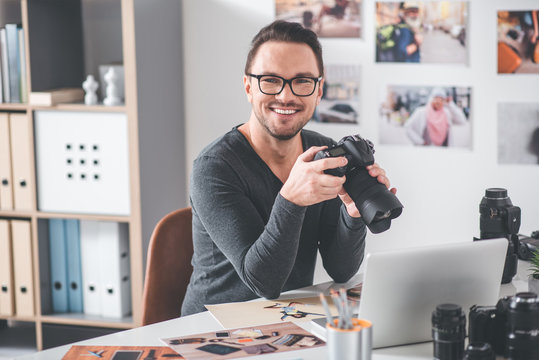 Portrait of smiling bearded man choosing pictures in camera while sitting at table in office. Work concept