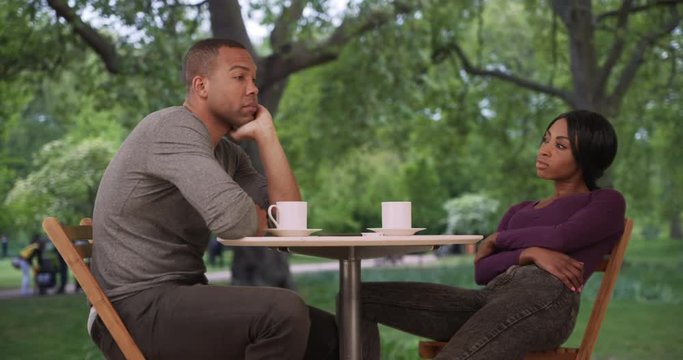Bored black couple drinking coffee sit quietly together at outdoor table