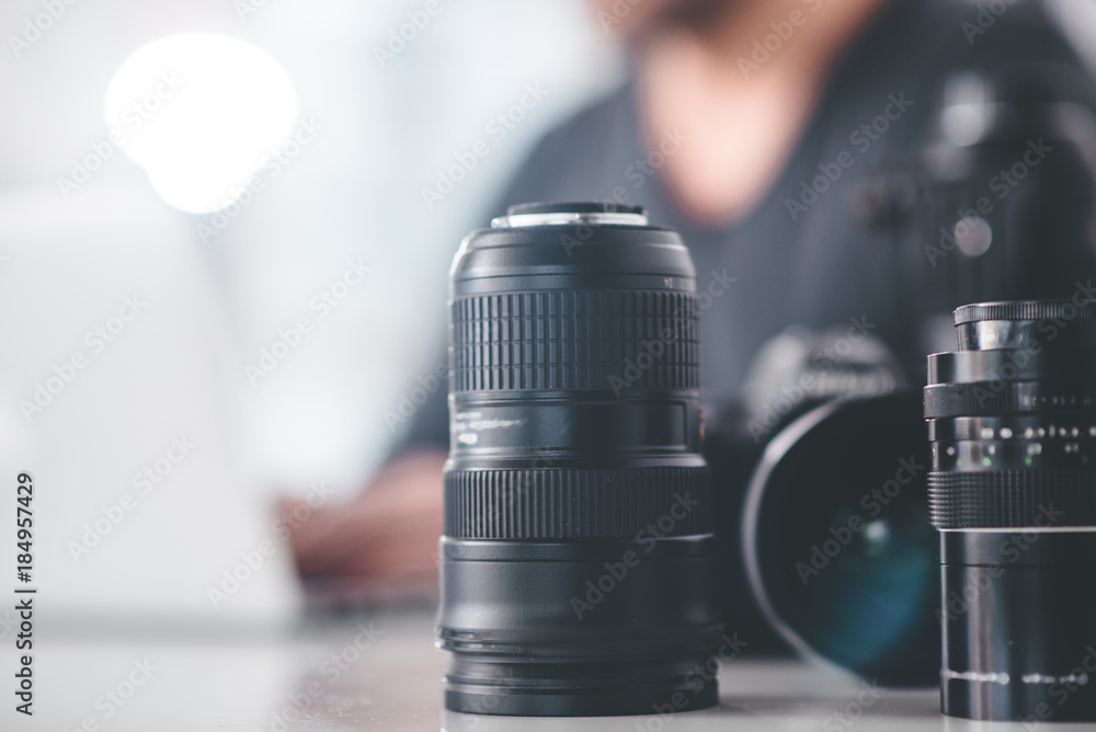 Poster close up of different photographic lens system locating on table. man having work with digital devic