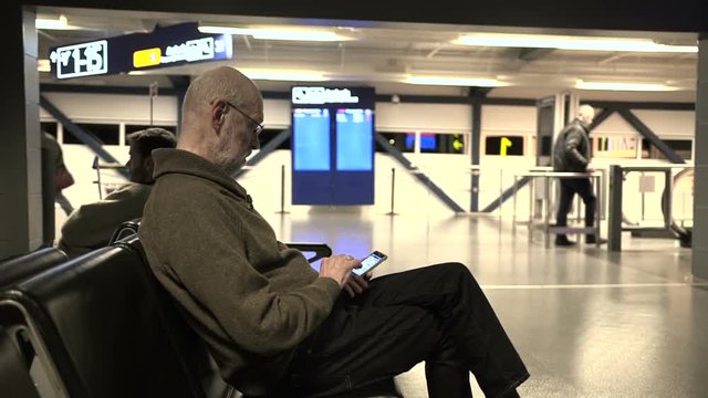Patient senior at Helsinki airport working with smartphone