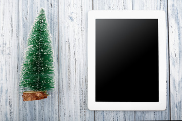 tablet and Christmas tree on light grey wooden background