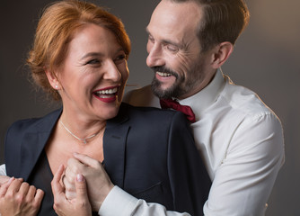 Portrait of joyful loving mature couple hugging and laughing. Caring gentleman is giving his jacket to lady with fondness. Isolated